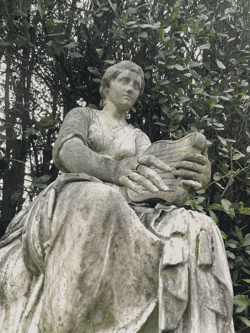 a low angle photo of a stone statue of a woman playing the lute amidst green trees